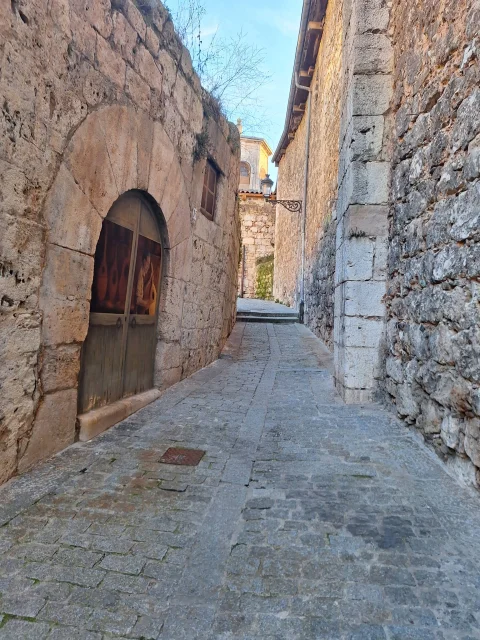 Vista en perspectiva de un estrecho callejón empedrado entre muros de piedra de aspecto medieval en la Calle Embajadores