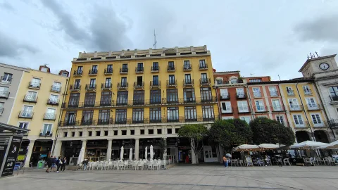 Fachada de edificio amarillo con balcones de hierro en la Plaza Mayor junto a terrazas