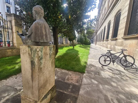 Vista posterior del busto de bronce de Juan Pablo II junto a la fachada y jardines exteriores de la Facultad de Teología