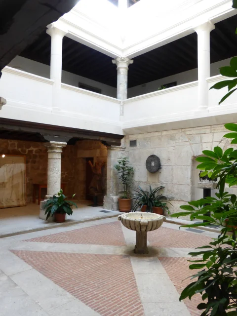 Patio claustrado de dos plantas con columnas de piedra, plantas decorativas y pila de piedra en el centro