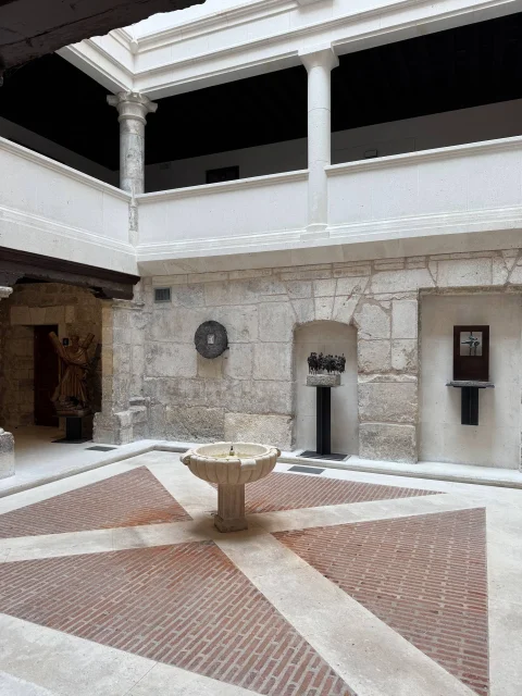 Patio interior porticado con suelo de ladrillo en espiga, pilares de piedra y una pequeña fuente tallada en el centro
