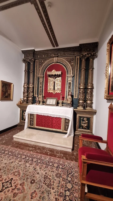 Pequeña capilla o oratorio con altar cubierto por mantel blanco, crucifijo, retablo de madera con columnas doradas