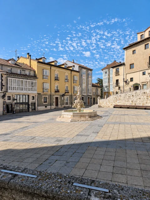 Explanada pavimentada con fuente en el centro rodeada de edificios de galerías acristaladas en Burgos