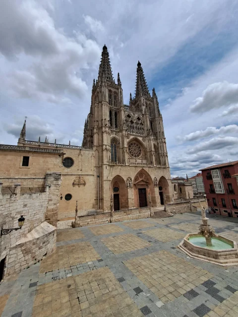 Vista en picado de la plaza empedrada con fuente octogonal frente a las torres de la catedral de Burgos