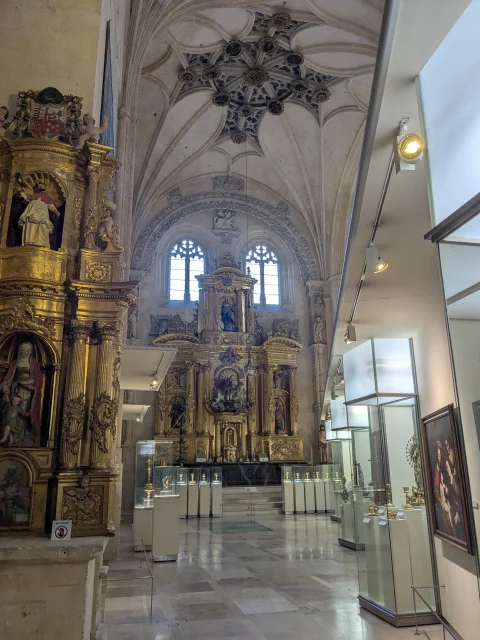 Vista axial de la capilla musealizada con retablos barrocos dorados y vitrinas exentas de orfebrería