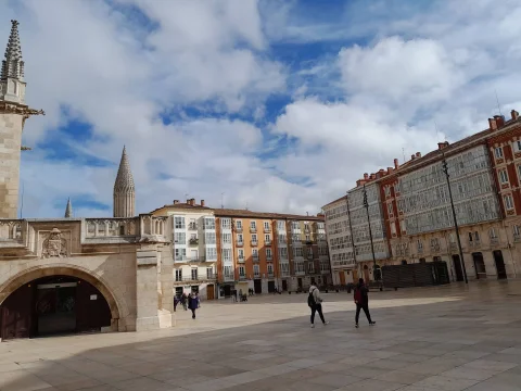 Vista de la plaza con viandantes en primer plano, arcos de la lonja catedralicia y caserío colorido al fondo