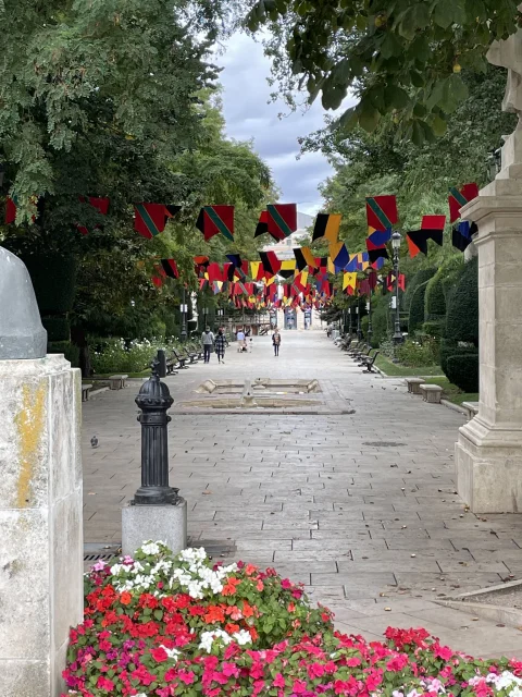Perspectiva festiva del paseo con banderolas de colores, flores en primer plano y estanque bajo