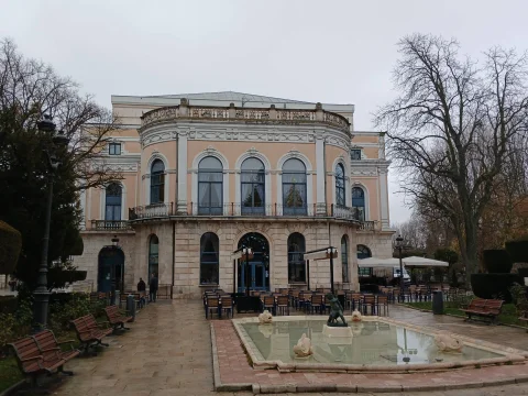 Vista frontal del Teatro Principal con la Fuente del Niño de la Oca y terrazas en día nublado