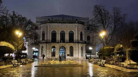 Vista nocturna de la Fuente del Niño de la Oca y el estanque iluminado ante el Teatro Principal lluvioso