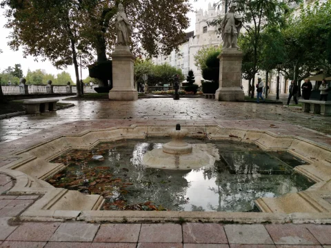 Estanque ornamental polilobulado en primer plano con las estatuas reales y el Arco de Santa María al fondo