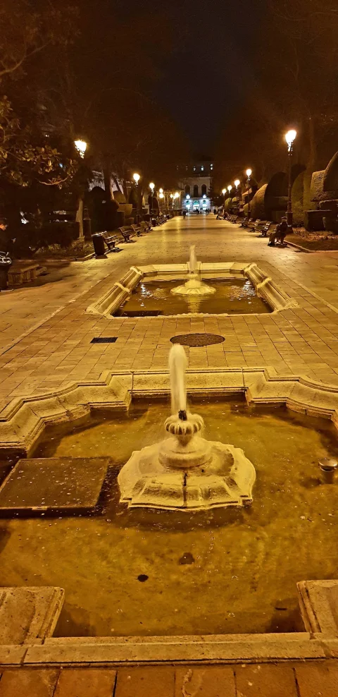 Perspectiva nocturna de los estanques ornamentales con surtidores de agua iluminados por farolas clásicas