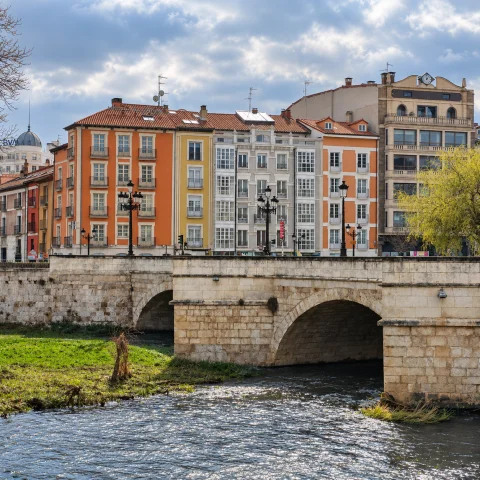 Arcadas de sillería de piedra sobre las aguas del río Arlanzón con el frente de edificios coloridos del Espoloncillo