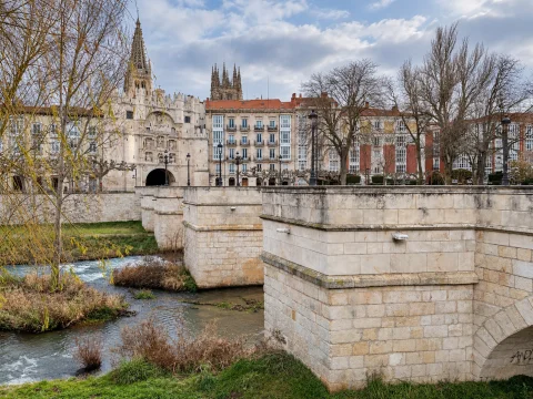 Estructura de sillería del puente sobre el cauce del río con el arco renacentista y agujas de la catedral al fondo