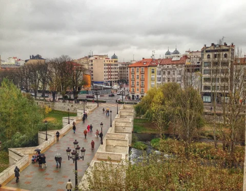 Vista aérea de la calzada peatonal del Puente de Santa María con viandantes bajo paraguas y farolas fernandinas