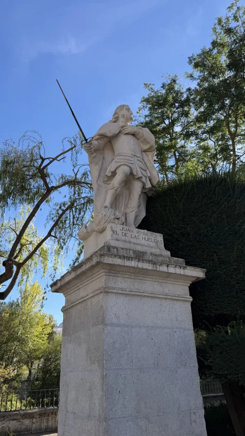 Estatua de piedra blanca del rey Juan I alzando una espada sobre un pedestal clásico