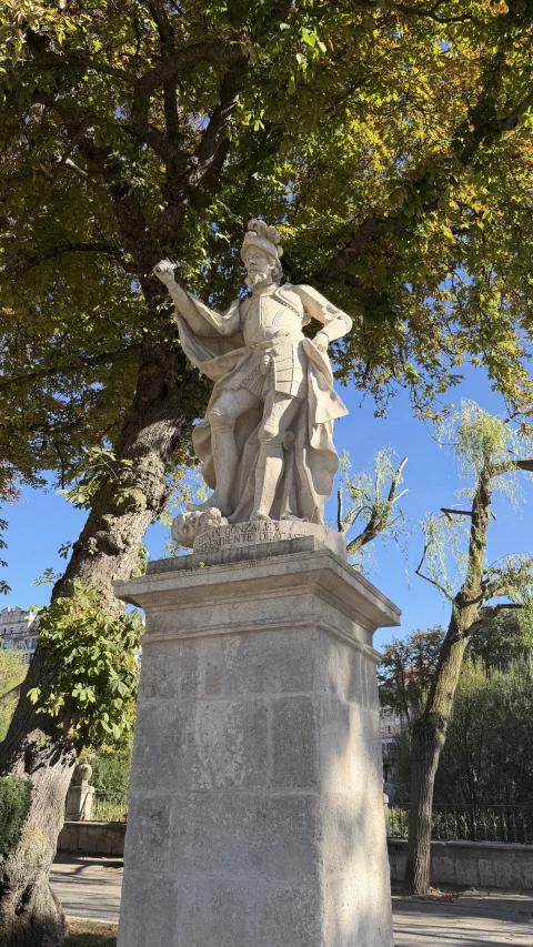 Estatua clásica de piedra de Fernán González con armadura y capa sobre alto pedestal