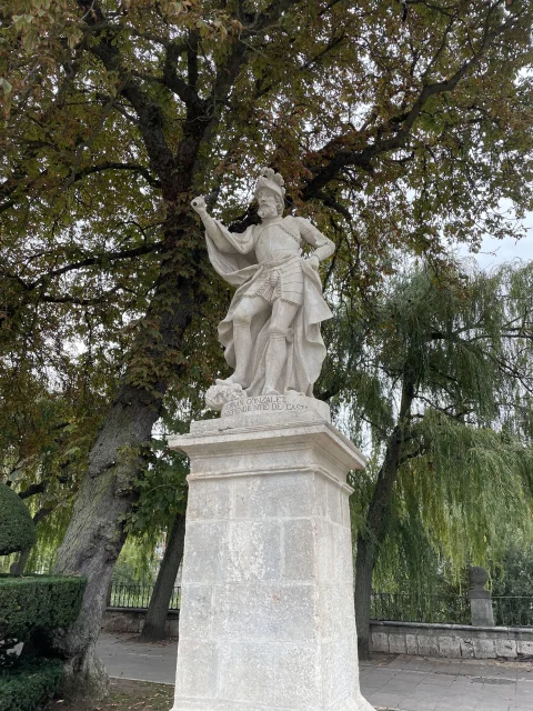 Estatua en piedra caliza del conde Fernán González sobre pedestal con el arbolado de ribera de fondo