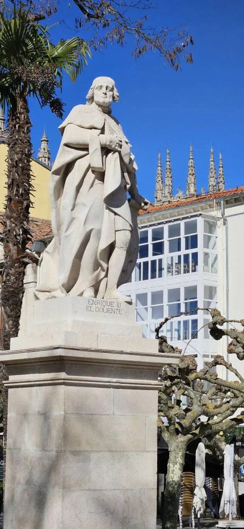 Estatua en piedra caliza de Enrique III «el Doliente» sobre pedestal con las agujas de la catedral al fondo