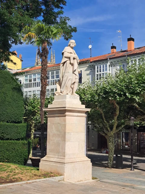 Vista de la escultura de Enrique III sobre alto pedestal de sillería entre palmeras y edificios del paseo