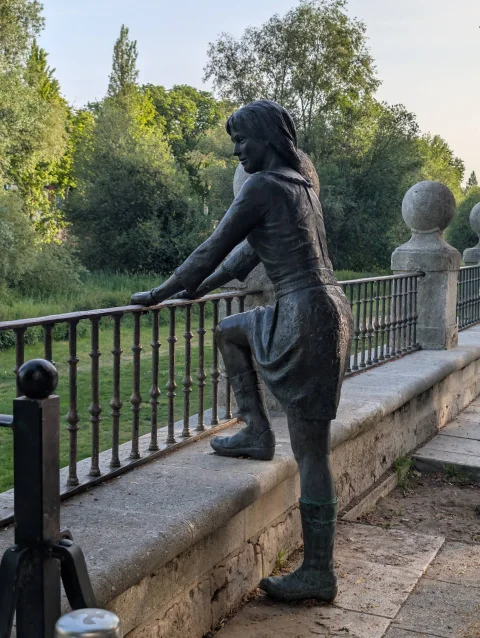 Escultura de cuerpo entero de La Niña de la Barandilla apoyada con una bota en el zócalo de sillería