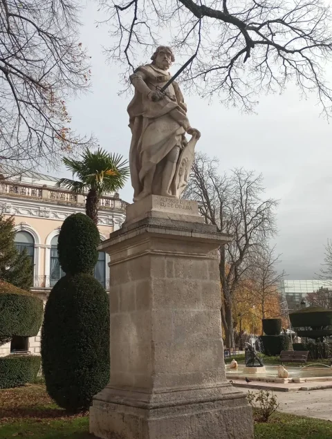 Perspectiva de la escultura de Alfonso VI sobre pedestal con seto cónico y estanque al fondo