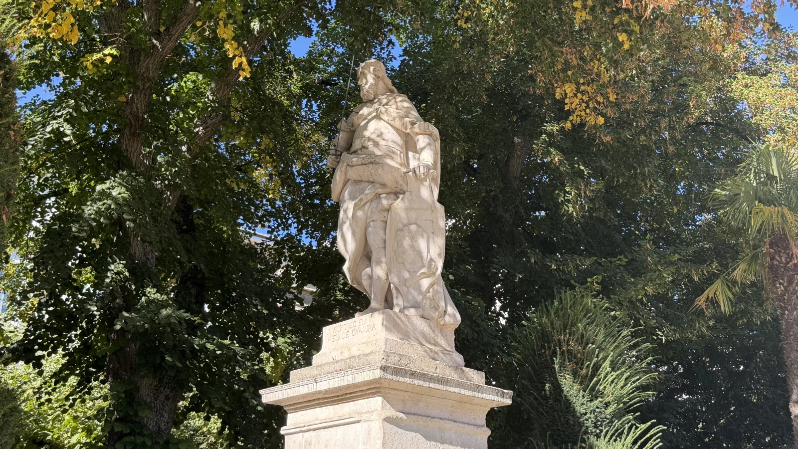 Estatua en piedra de Alfonso VI sobre pedestal en parterre ajardinado