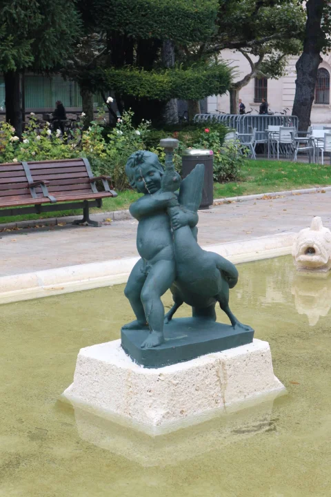 Escultura en bronce del Niño de la Oca sobre plinto de piedra en el estanque ornamental con pez esculpido