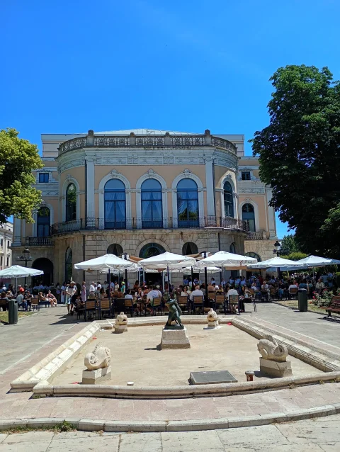 Estanque seco de la Fuente del Niño de la Oca con peces esculpidos y terrazas concurridas ante el Teatro Principal