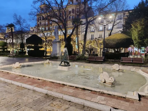 Vista crepuscular de la Fuente del Niño de la Oca con estanque iluminado, surtidores y arbolado nocturno