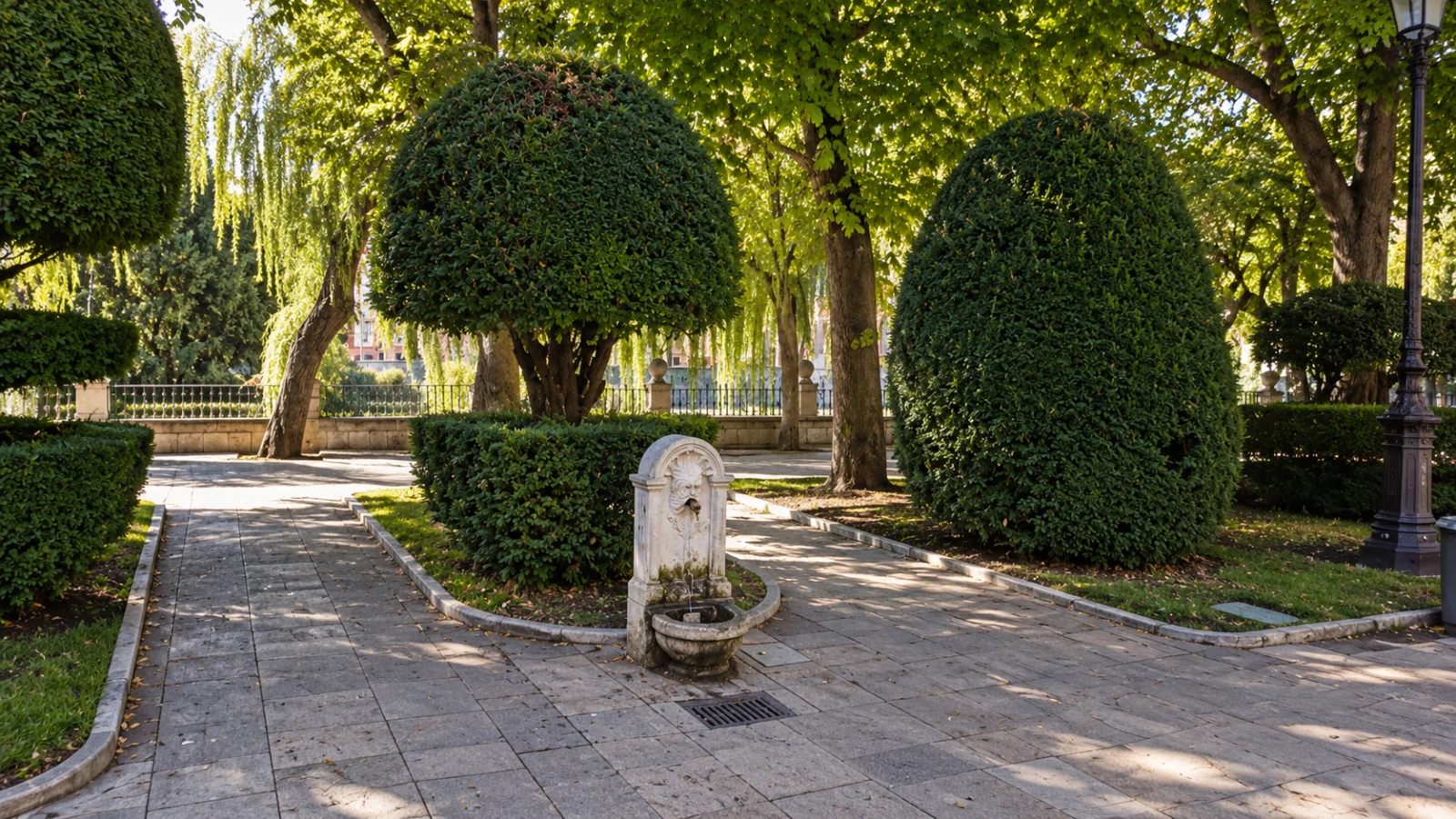 Fuente de piedra con mascarón tallado integrada entre setos topiarios y sauces de la ribera