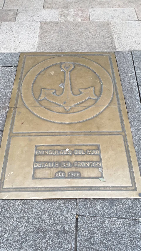 Placa conmemorativa de bronce en el suelo con el ancla del frontón del Consulado del Mar (1796)