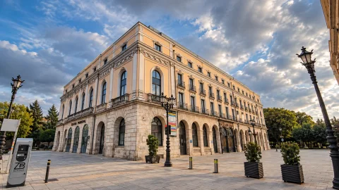 Edificio de teatro clásico en esquina con arquerías inferiores, farola de forja y cielo con nubes doradas