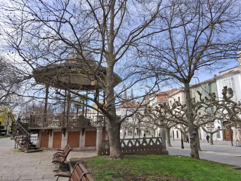 Árboles altos sin hojas enmarcando el quiosco de música y bancos de parque sobre el paseo empedrado