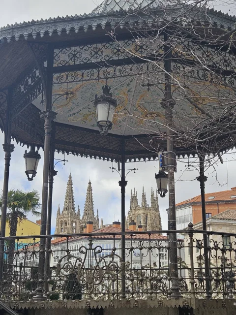 Detalle de la barandilla de hierro y farolas del templete con las torres de la catedral de fondo
