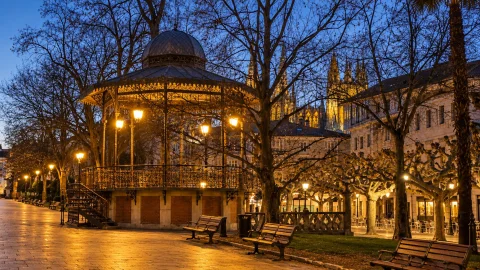 Templete de música iluminado con farolas de noche en paseo arbolado con agujas góticas de la catedral detrás