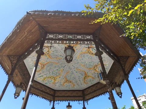 Vista cenital del techo octogonal decorado con pinturas modernistas y farol central en el quiosco de música