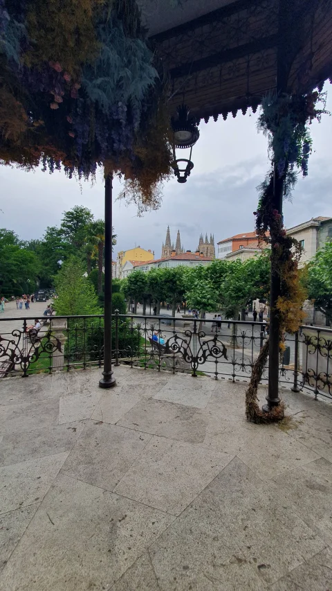 Vista desde el interior del quiosco adornado con flores hacia el paseo arbolado y agujas lejanas
