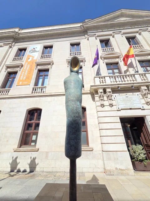 Escultura moderna de un monje de bronce sobre pedestal frente al edificio neoclásico de la Diputación Provincial