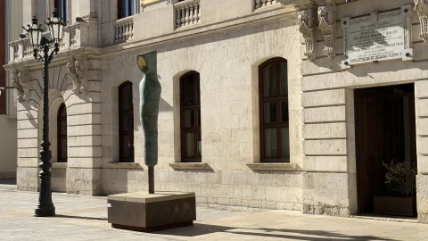 Vista angular de la escultura de bronce junto a una farola fernandina y los ventanales de la Diputación