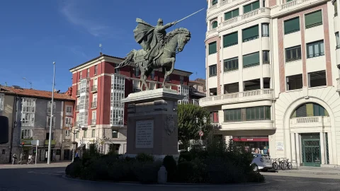 Estatua ecuestre de bronce sobre pedestal clásico en una rotonda ajardinada frente a edificios urbanos