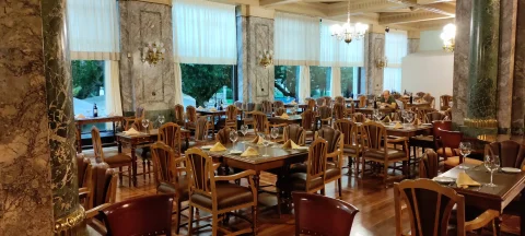 Comedor noble con mesas dispuestas, columnas de mármol verde, apliques clásicos y ventanales al paseo