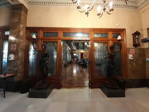 Doble escultura de bronce sosteniendo lámparas de fuego a los lados de una puerta con vidrieras emplomadas