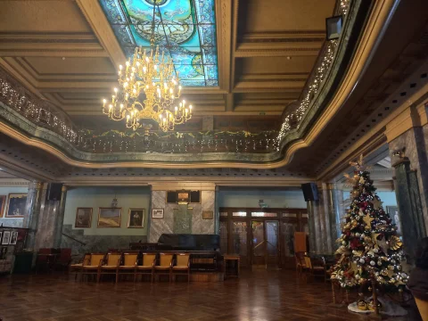 Gran salón noble decorado de Navidad con árbol iluminado, lucernario polícromo y araña dorada