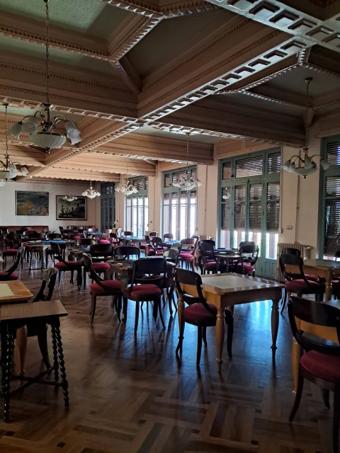 Perspectiva del salón social con artesonado de vigas decoradas, mesas de juego y grandes ventanales con persianas