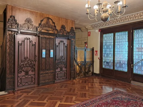 Puertas de ascensor con cancelas modernistas de forja, lámpara dorada y cristaleras emplomadas