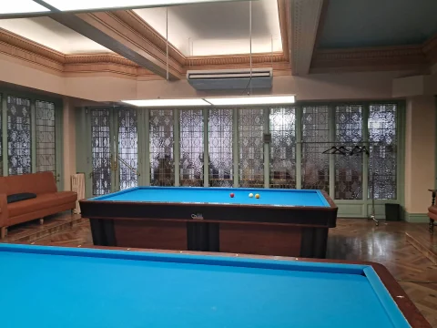Sala de billar francés de paño azul enmarcada por ventanales de cristalera translúcida y techo artesonado