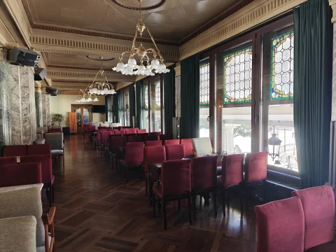 Salón señorial con suelo de parqué en espiga, butacas de terciopelo rojo, vidrieras emplomadas y lámparas de araña