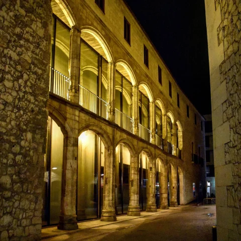 Arquería porticada iluminada de noche con acristalamiento moderno que integra el centro cultural