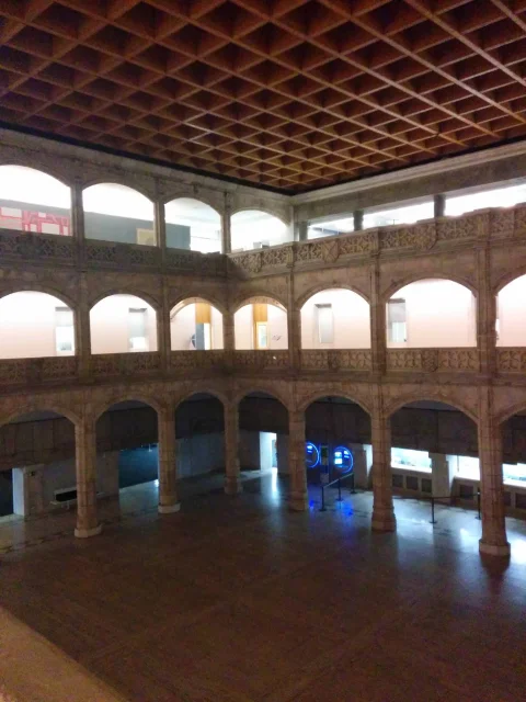Vista en ángulo elevado del patio renacentista iluminado, mostrando el artesonado o cubierta cuadriculada