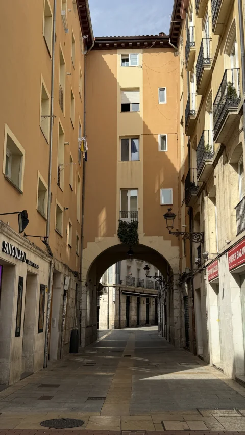 Vista en profundidad de la calle peatonal que atraviesa el arco bajo un edificio residencial de tono ocre